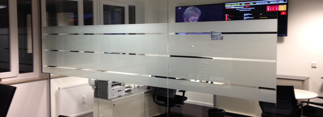 Glaswand mit satinierten Sichtschutzstreifen im Büro mit Monitoren und Arbeitsplätzen.
